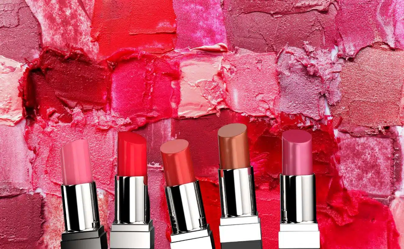 Lipstick display with vibrant red and pink shades against a textured, colorful lipstick smudge background.