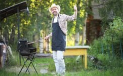 Grilling outdoors in a backyard garden with a man wearing a hat and apron, giving a thumbs-up during a sale event. Perfect for promoting outdoor cooking and BBQs.