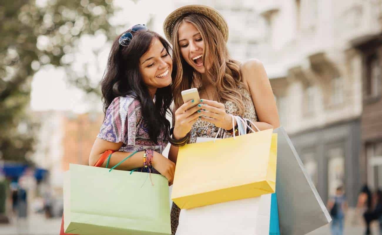 Consumers enjoying shopping during a sale event, looking at a smartphone for deals.