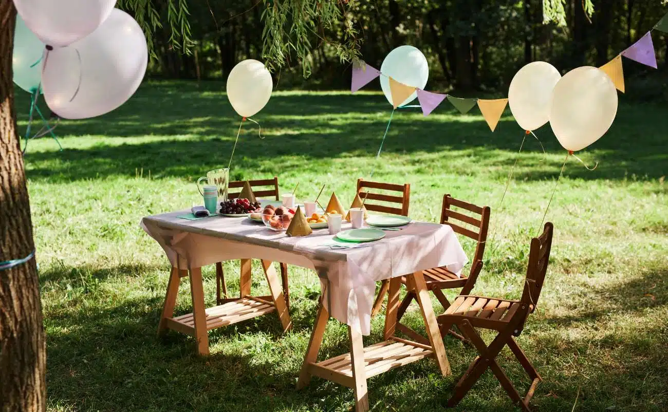 Colorful outdoor birthday party setup on a sunny garden lawn with decorated table, balloons, and party favors.