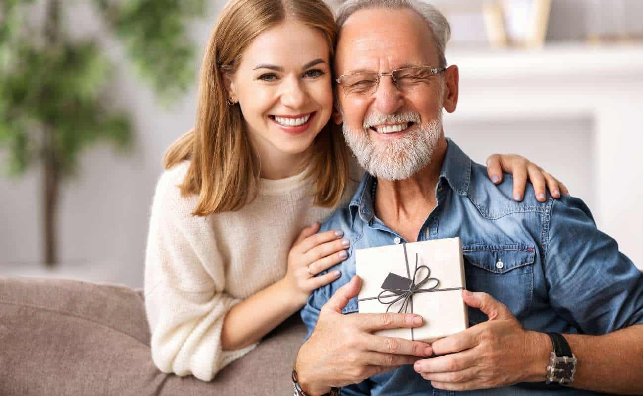 Happy elderly man receiving gift from smiling young woman during Sale is Live event, showcasing joyful shopping and special offers.
