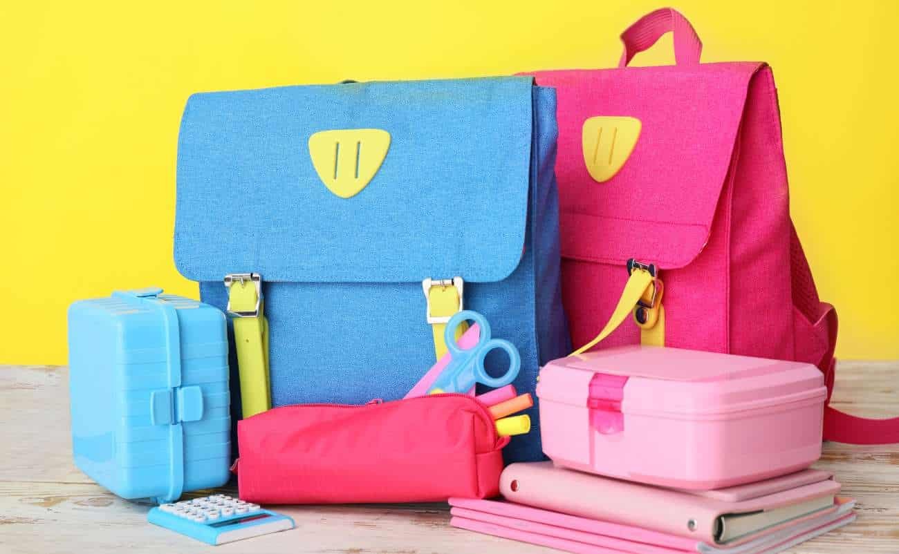 Bright colorful backpacks, stationery, and school supplies on a wooden surface with a yellow background, promoting back-to-school sales and discounts.