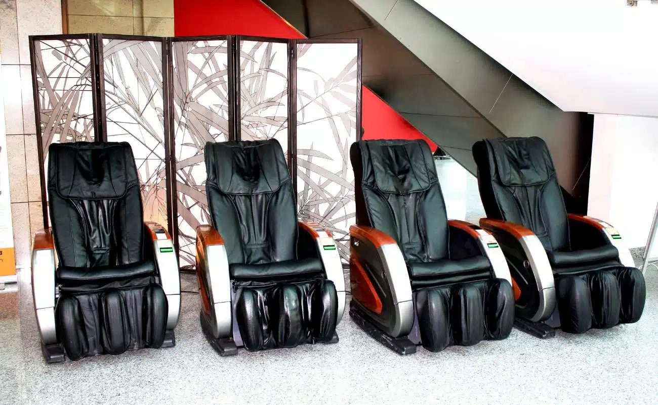 Black massage chairs at sale event, near decorative folding screen, in modern public space.