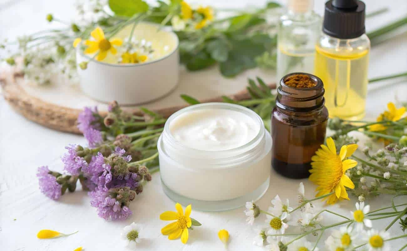 Botanical skincare products with essential oils, herbal creams, and natural remedies on a white surface with fresh flowers for health and wellness.