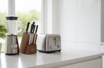 A modern kitchen countertop featuring a stainless steel blender, a wooden knife block with multiple knives, and a toaster, all arranged neatly near a window with natural light.
