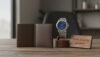 Elegant wristwatch, wallet, and personalized gift on a wooden desk.