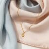 Elegant gold necklace with a round pendant, perfect for Mother's Day gift, displayed on soft pastel silk fabric.