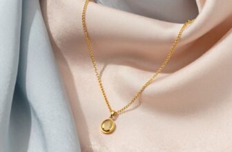 Elegant gold necklace with a round pendant, perfect for Mother's Day gift, displayed on soft pastel silk fabric.